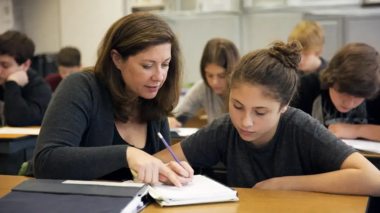 Teaching assistant helping a middle-school student with classwork in a Canadian classroom